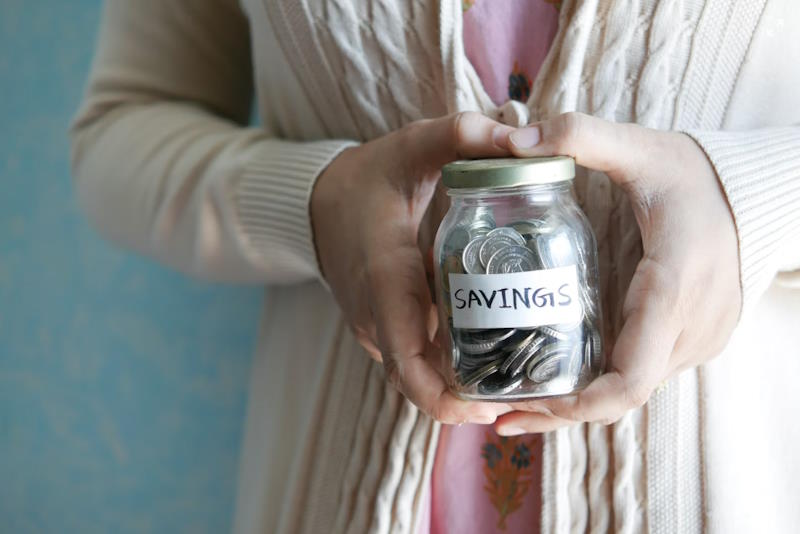 woman holding a glass jar with coins and a savings label